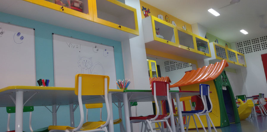 mesas e cadeiras infantis coloridas, quadros brancos afixados na parede, armáriosd coloridos afixados na parede com brinquedos e uma casa infantil colorida