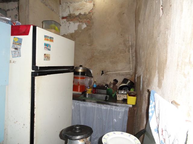 Cozinha com paredes sem pintura, uma geladeira e uma pia com diversos itens de cozinha.