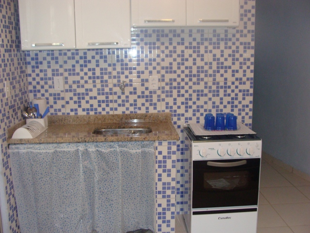 Cozinha com paredes de piso quadriculados em detalhes azuis e brancos, um armário suspenso branco com quatro portas, um fogão e uma pia com utensílios de cozinha.