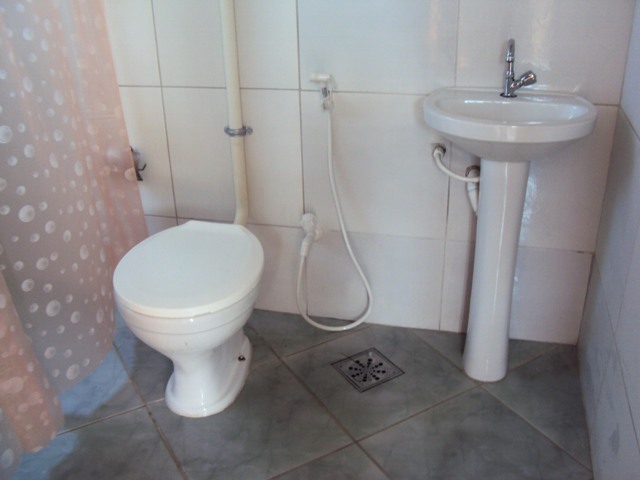 Banheiro com parede de piso branco, com vaso sanitário, pia e uma cortina de bolinha.
