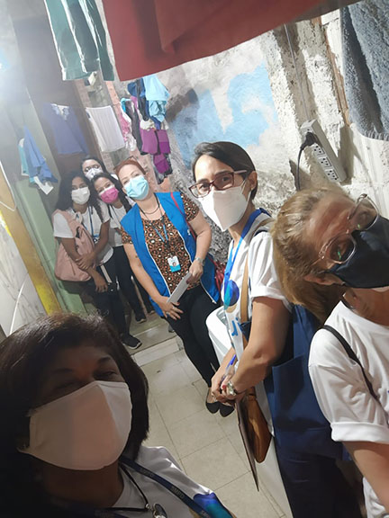sete mulheres num corredor com paredes de casas descascadas e sem pintura