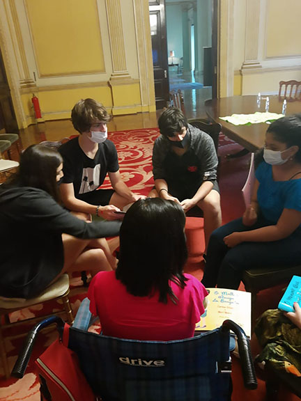 grupo de jovens com e sem deficiência sentados em círculo manuseando livro e conversando