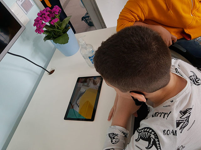 menino de blusa branca observando um tablet que se encontra sobre uma mesa branca