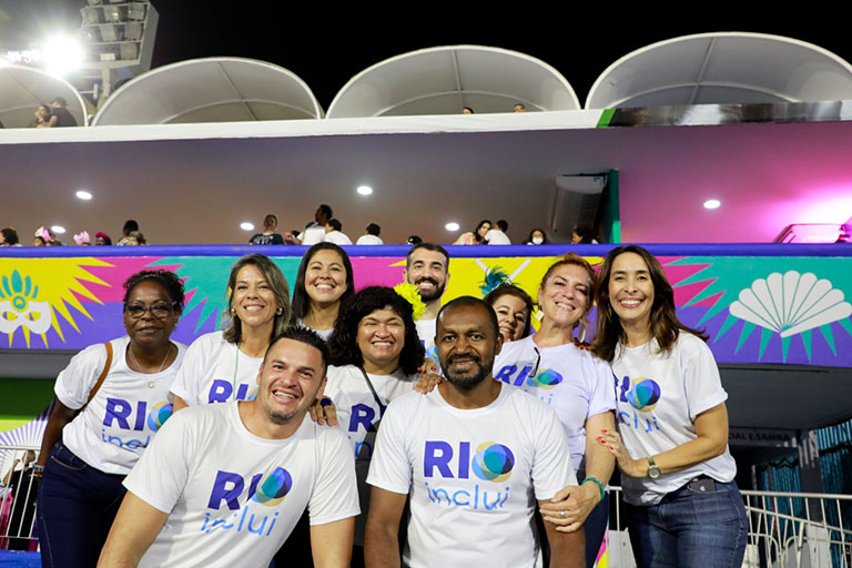 equipe RIOinclui composta por dez pessoas. Todos sorridentes. Camarote colorido do Sambódromo ao fundo