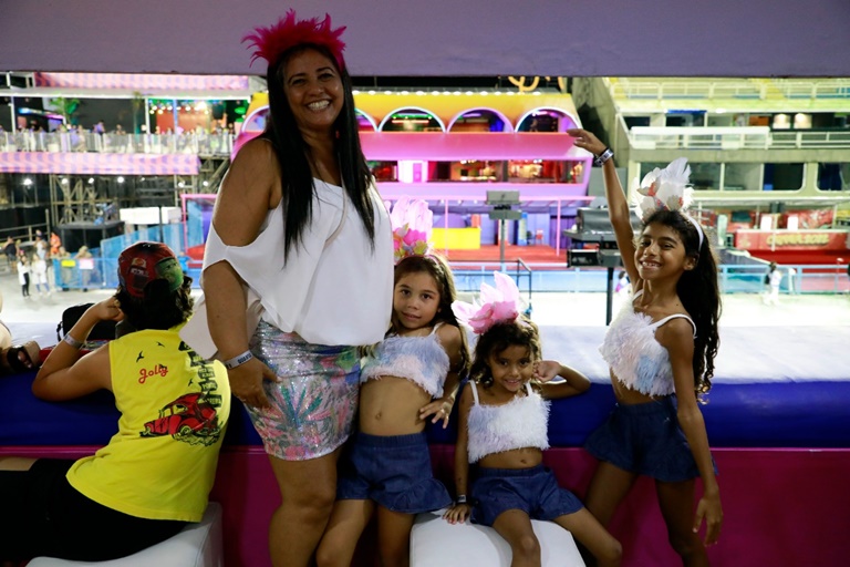 mulher sorridente com alegoria de carnaval acompanhada de Três crianças sorridentes e um adolescente no camarote do sambódromo