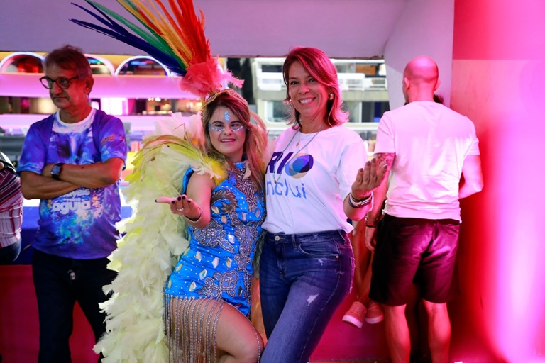 duas mulheres de estatura mediana, com roupas coloridas posando para a foto no camarote do sambódromo