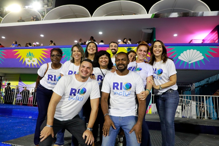 equipe RIOinclui composta por dez pessoas. Todos sorridentes. Camarote colorido do Sambódromo ao fundo