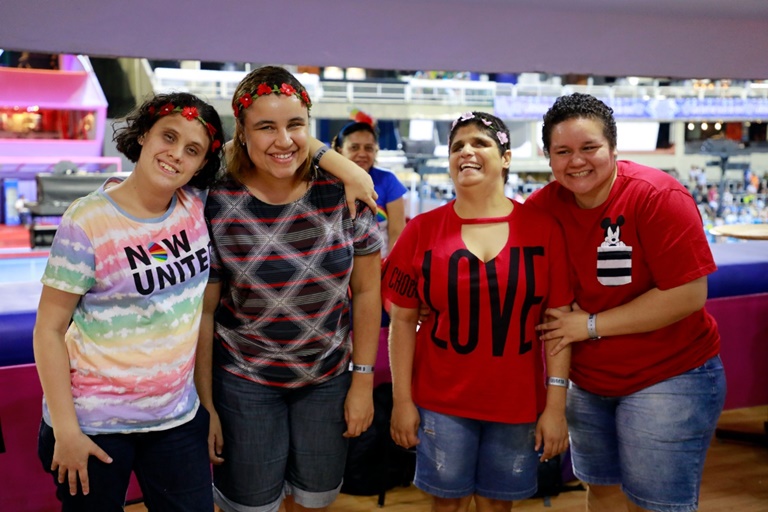 quatro mulheres com deficiência visual sorridentes. Sambódromo ao fundo