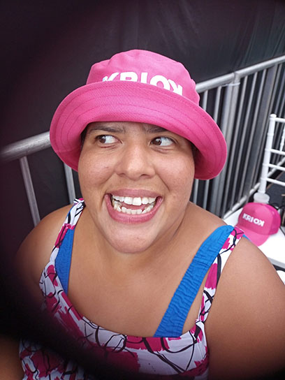 Uma mulher sorrindo para foto, com chapéu do evento KRIOK.