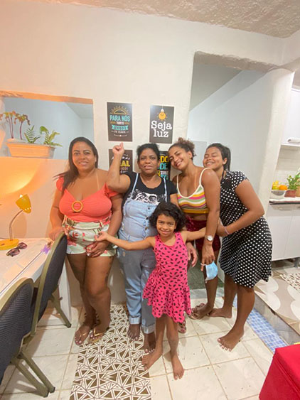 Família sorrindo para foto dentro da casa reformada pelo Programa Moradia e Acesso, ao fundo uma parede branca com quadros.